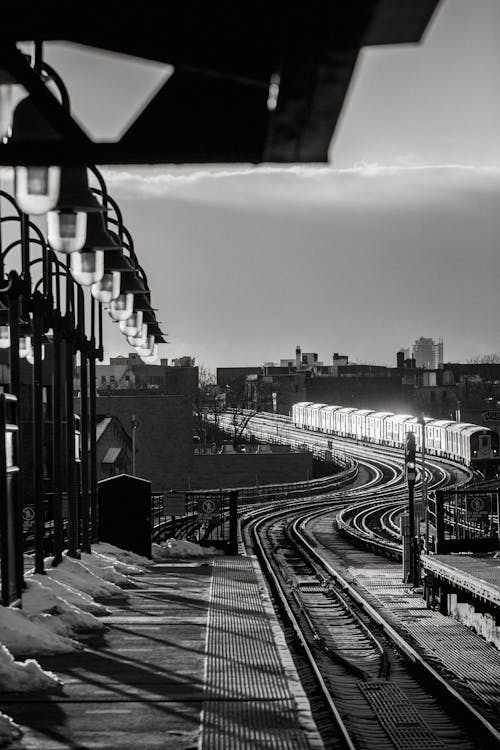 Black and white of train riding on railway tracks on railroad station near platform with snow and streetlights in city