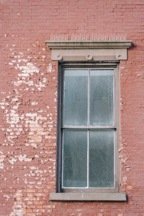 Dark unwashed window located on shabby red brick wall of old residential building