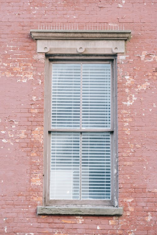 Fragment of exterior of aged red brick building with shabby wall and narrow window with shutters