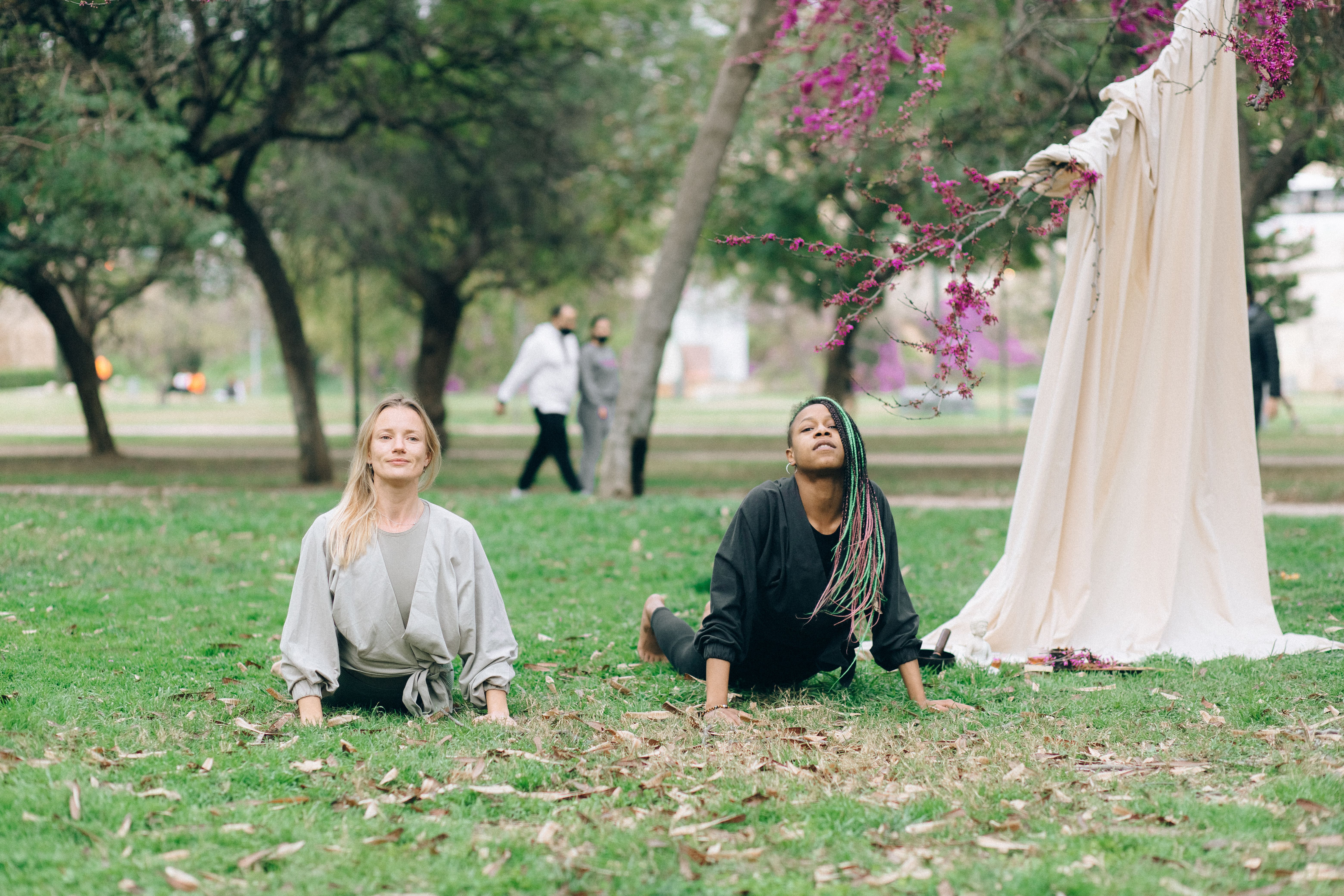 Two women practicing yoga outdoors in a tranquil park environment, embracing wellness and mindfulness.
