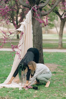 Two women practice yoga poses outdoors surrounded by beautiful pink blossoms, embodying wellness and tranquility.