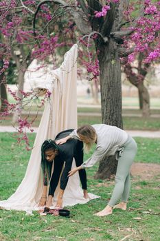 Two women practicing yoga outdoors under blooming trees, focused on stretching and wellness.