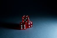 三个红色透明骰子堆叠在黑暗表面，突显了它们光滑的反射面和圆点