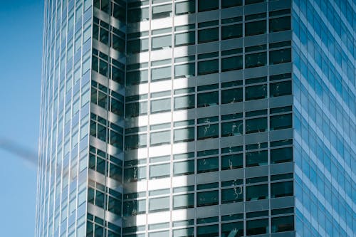 Low angle exterior of modern high rise city building with unusual geometric design and glass windows with sunlight and shadows