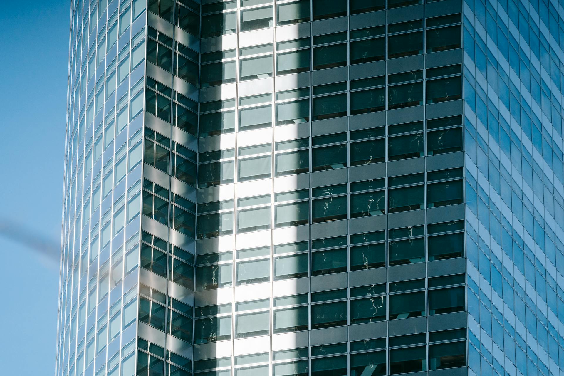 Low angle exterior of modern high rise city building with unusual geometric design and glass windows with sunlight and shadows