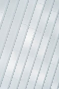 From below of symmetric white ribs and windows on walls of creative modern building in sunlight as abstract background