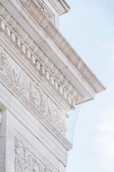 From below of bas reliefs and carved ornaments on marble facade of historical Washington Square Arch under cloudy blue sky in New York