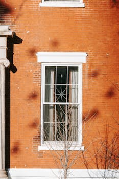 White window with grids of facade of classic styled brick building on sunny day in city