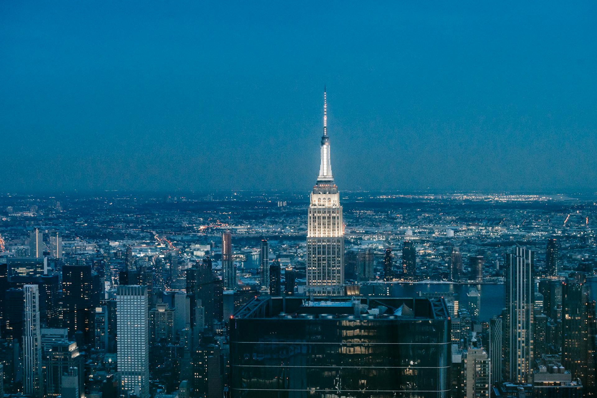 High tower with glowing lights located in downtown of New York city among glass buildings at night