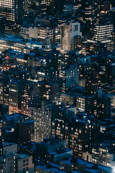 From above of modern tall houses with bright glowing lights located on dark streets of contemporary megapolis at night time