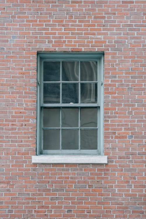 Fragment of old brick dwelling building with rectangle window in painted wooden frame