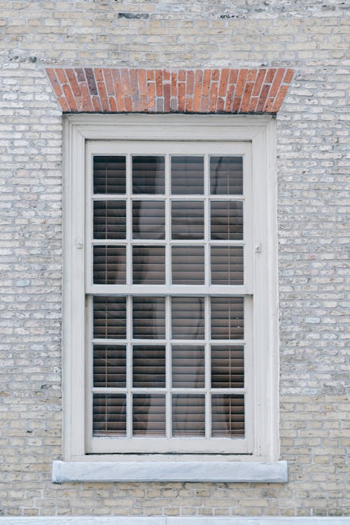 Facade of aged brick apartment building with window in wooden frame shut with blinds
