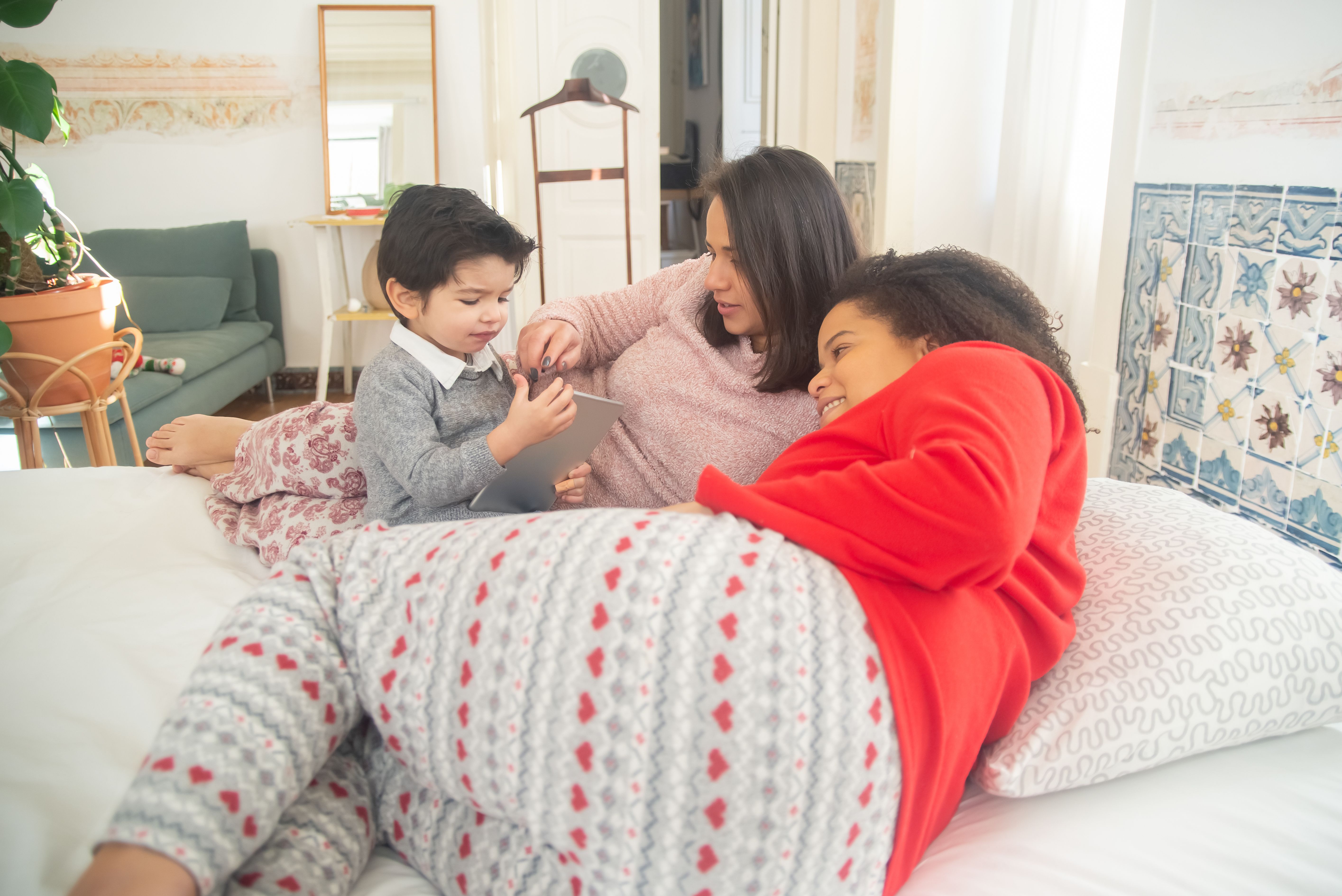 A loving family enjoying togetherness with a digital tablet in a cozy bedroom setting.