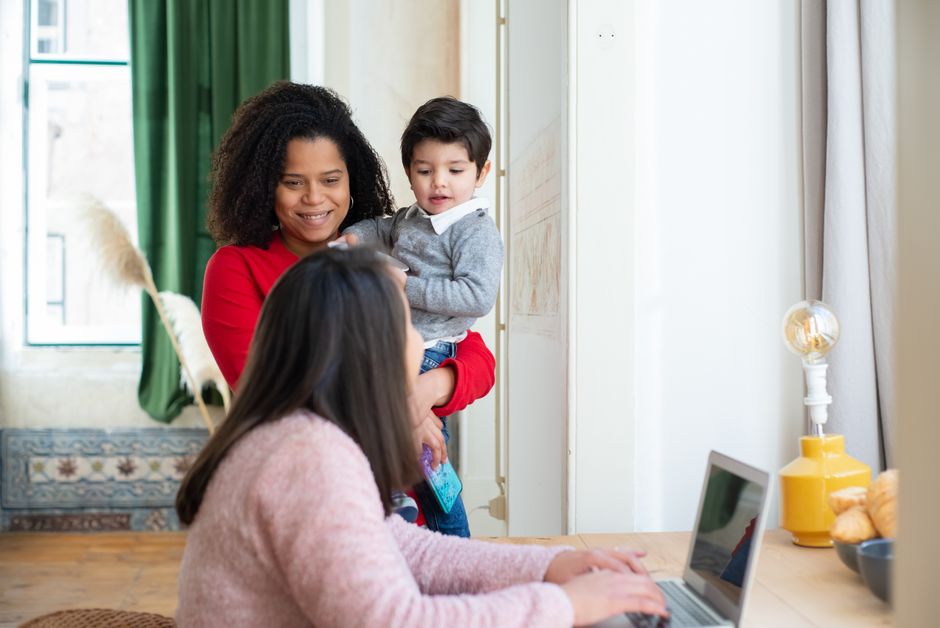 Pareja lesbiana con niño disfrutando del tiempo en familia en casa, usando un portátil.