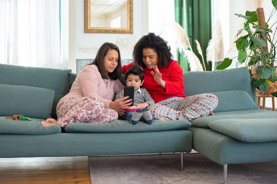 Lesbian couple and young boy enjoying time together on sofa with smartphone indoors.