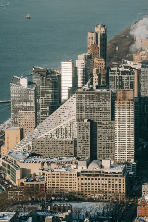 Free Contemporary skyscrapers and residential houses located on embankment of modern city with road and trees near calm water of sea Stock Photo