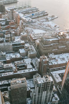 Drone view of tall modern residential houses located on snowy waterfront near calm sea in city on cold winter day