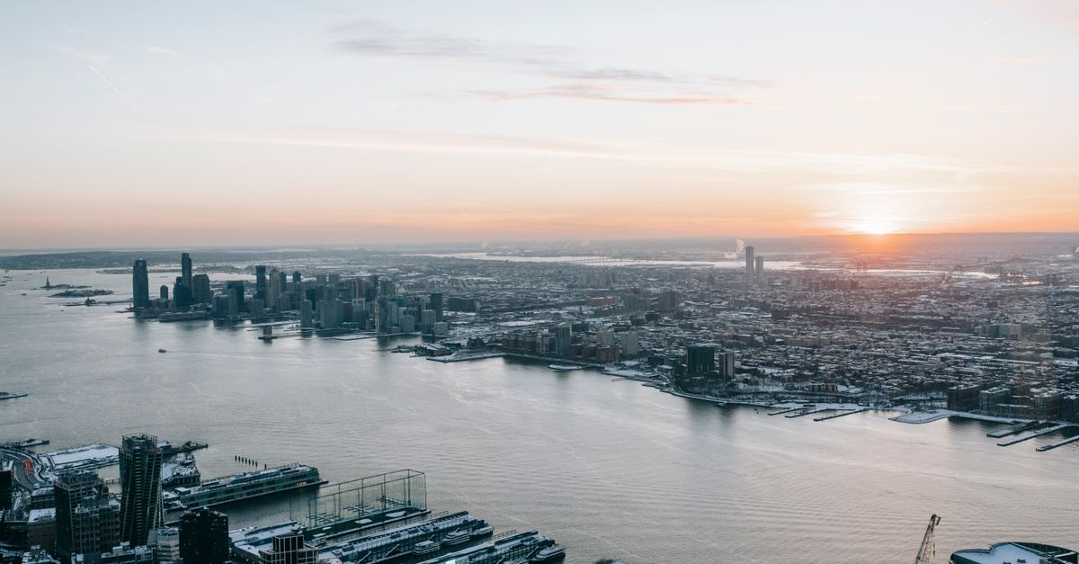 Calm sea flowing between modern coastal district of modern city with houses against sun setting on horizon in evening time