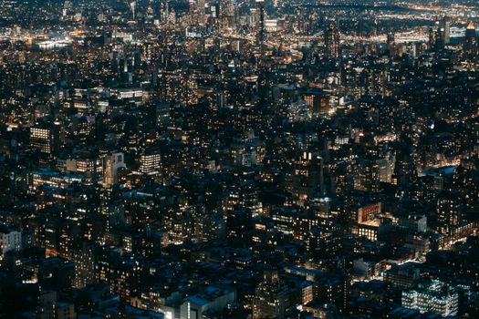 Drone view of modern multistory buildings with glowing lights located on dark streets of contemporary city at dark night time