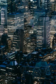 Contemporary high rise buildings and houses with glowing lights located on dark streets of modern city at dark night time