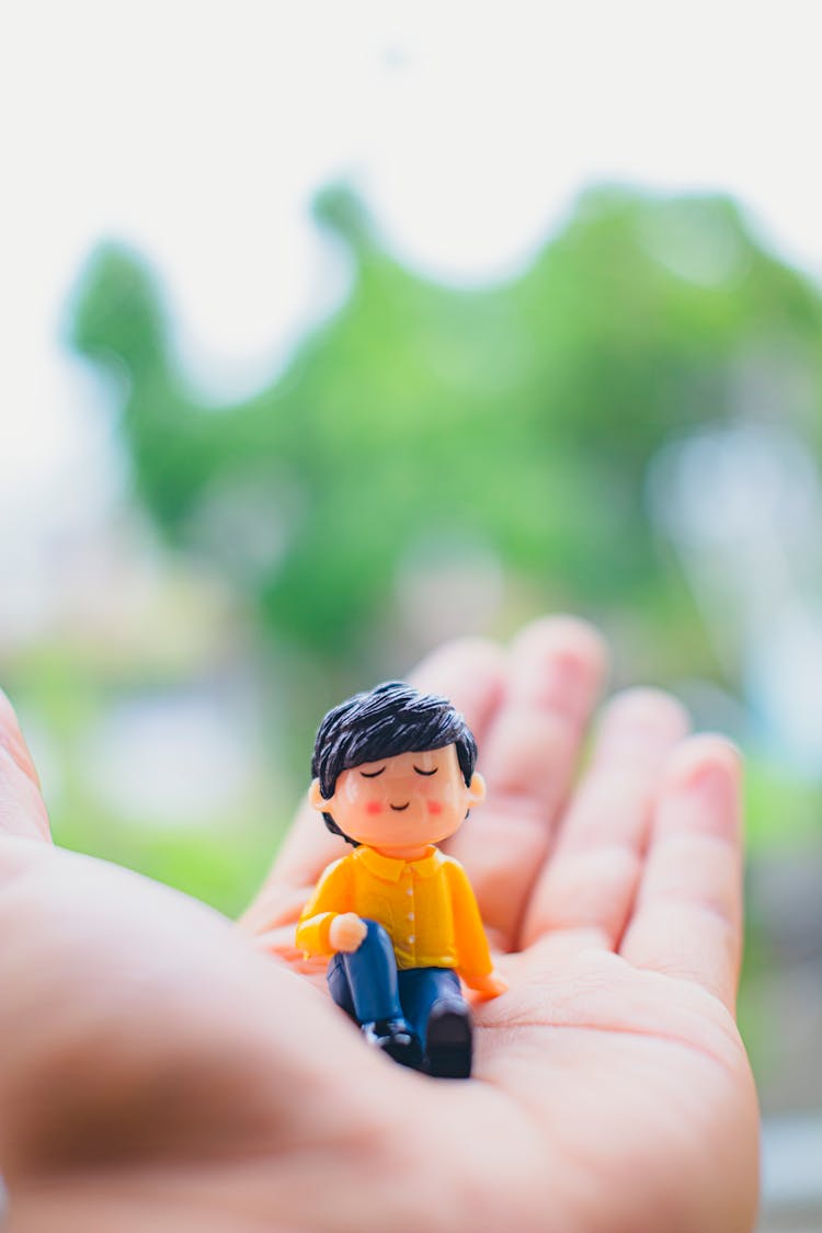 Crop Person Showing Statuette Of Man In Daylight