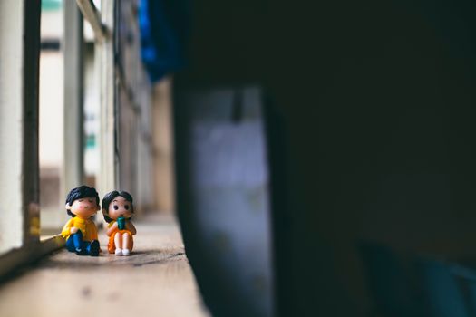 Small plastic figures of man with female beloved sitting on wooden windowsill in daytime on blurred background