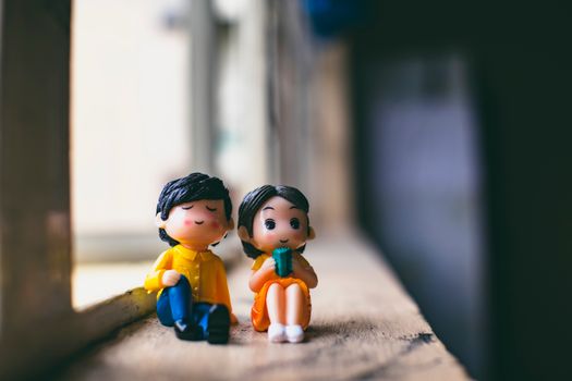 Plastic figures of man in colorful wear near girlfriend sitting against window in aged building on sunny day