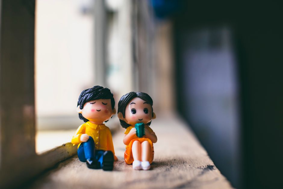 Plastic figures of man in colorful wear near girlfriend sitting against window in aged building on sunny day