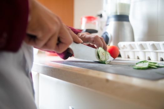 Close-up of a person slicing cucumbers on a kitchen counter for a healthy meal prep.