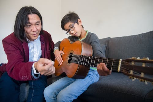 A Music Teacher Teaching a Boy How to Play a Guitar