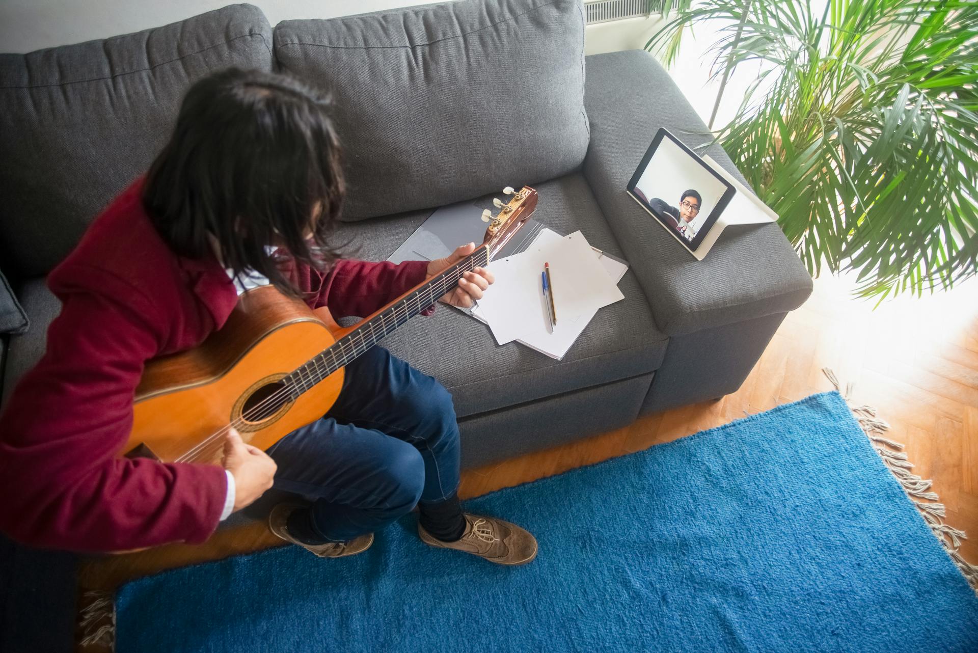 A man learning guitar online at home using an acoustic guitar and tablet.