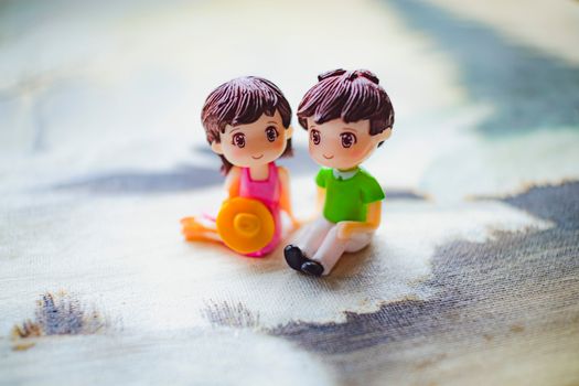 Statuettes of couple holding hands while sitting on artwork of sandy beach against ocean during summer trip