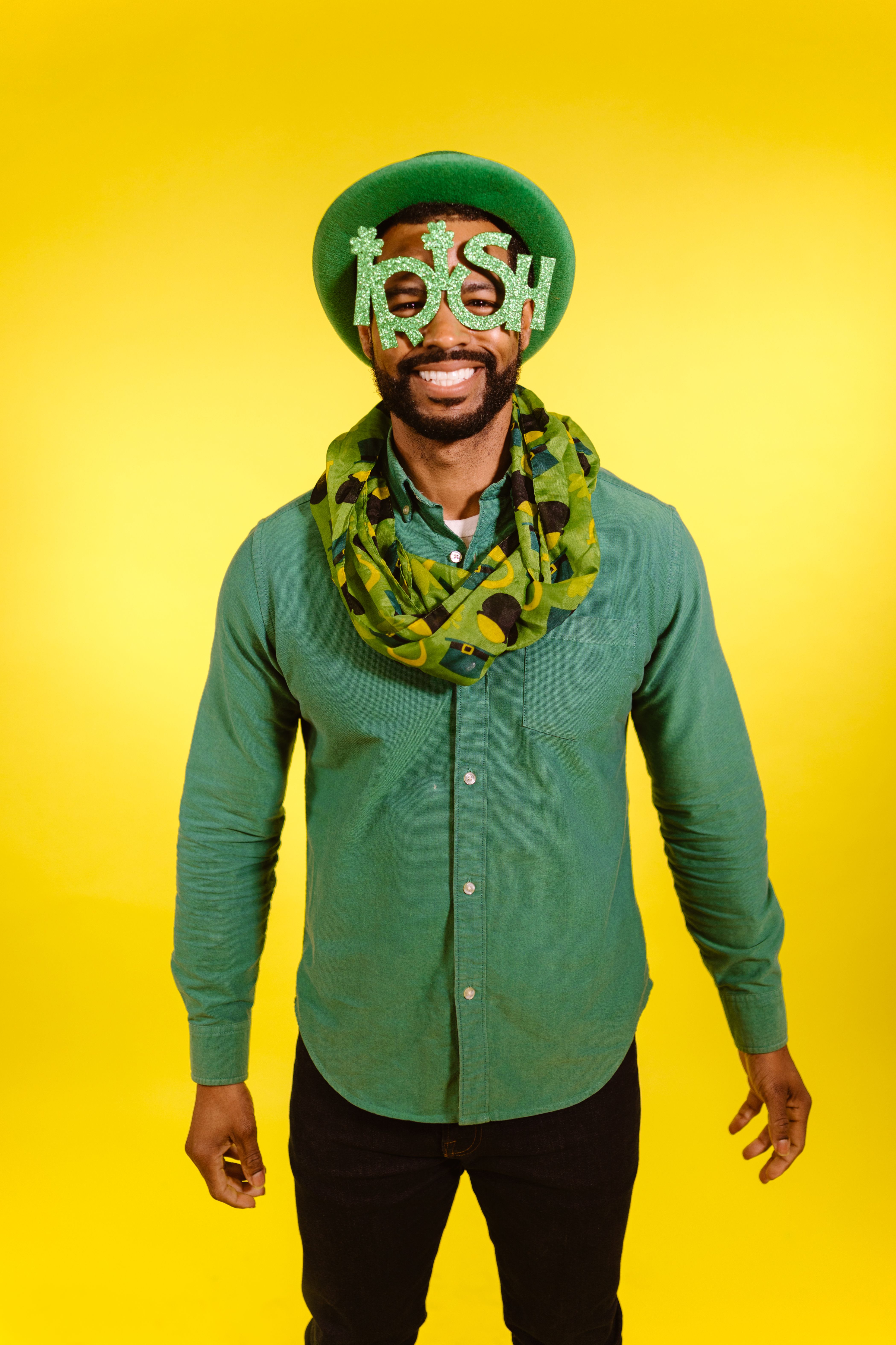 A man in playful Irish-themed attire celebrates St. Patrick's Day against a vibrant yellow background.