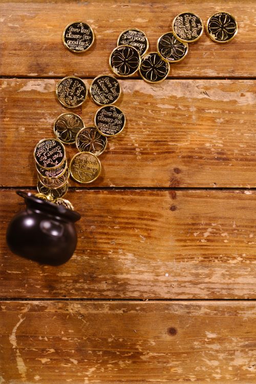 Free Overhead view of gold coins pouring from a black pot on a rustic wooden background, celebrating Saint Patrick's Day. Stock Photo