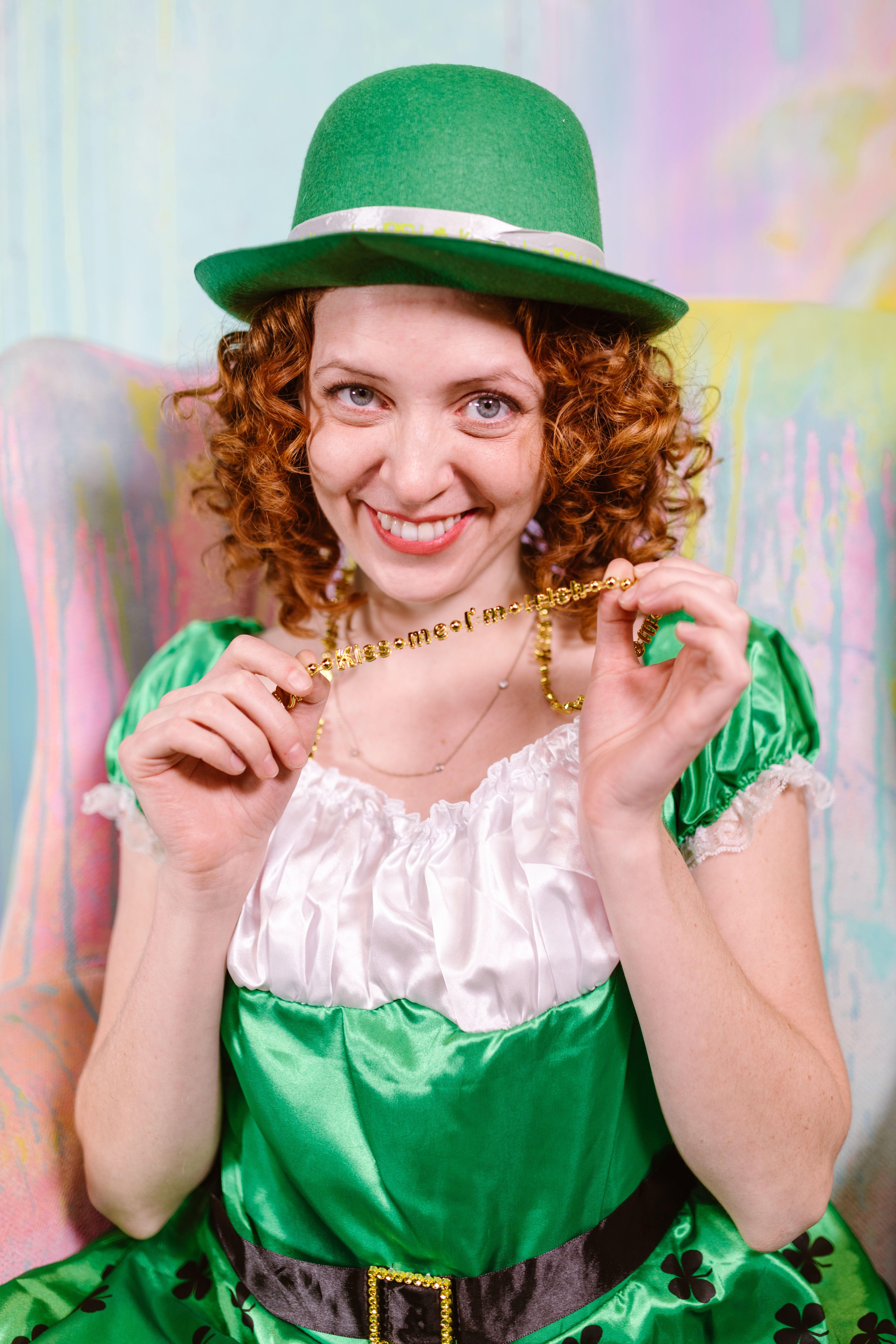 Smiling woman in green costume with hat celebrating St. Patrick's Day indoors.