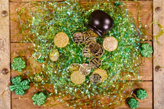 Overhead view of gold coins and shamrocks celebrating St. Patrick's Day with festive green tinsel.