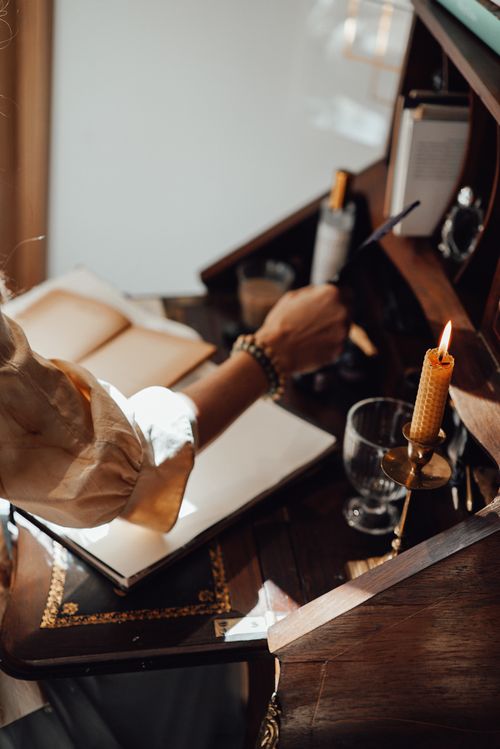 Free Crop unrecognizable female writer with feather against empty notepads and burning beeswax candle on vintage table in sunlight Stock Photo