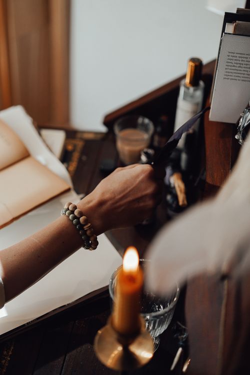 Free High angle of crop unrecognizable female author with feather at vintage table with notebooks and burning candle in house Stock Photo