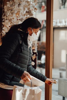 Woman in mask shopping indoors, holding bags during pandemic