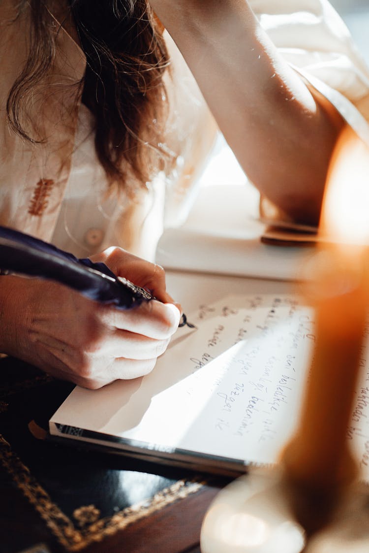 Faceless Author Writing Novel In Notepad With Feather In Sunbeam