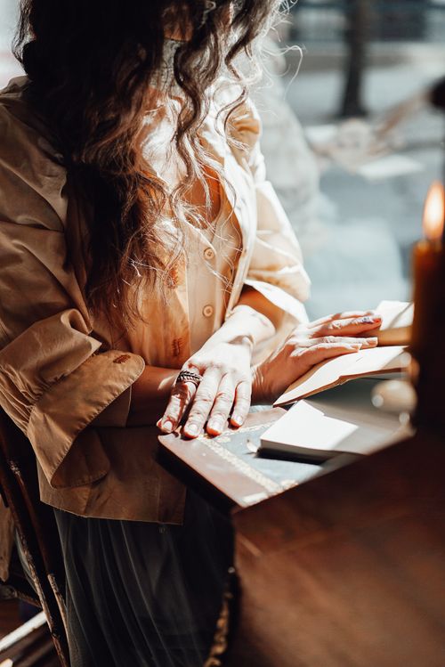 Free Crop unrecognizable female in retro blouse sitting at old table with notepad reflecting in glass wall in sunlight Stock Photo
