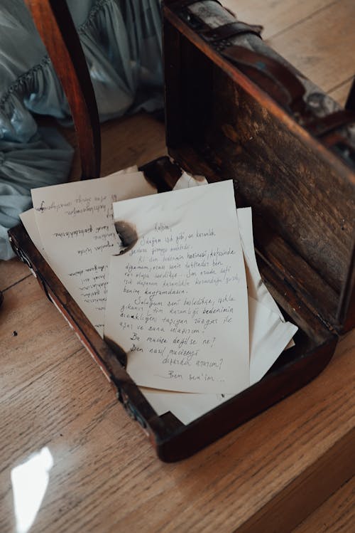 Free From above of opened aged suitcase with abundance of ink letters with burnt edges placed on wooden floor in room Stock Photo