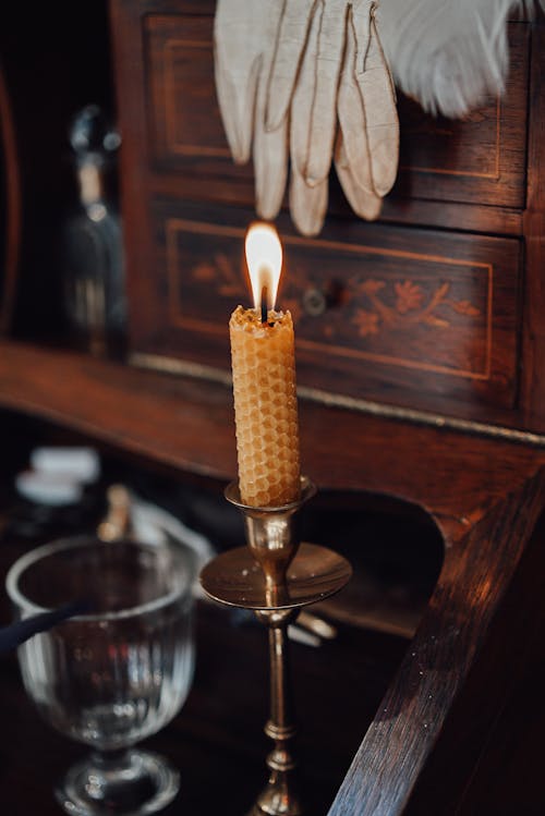 Free Burning candle placed on antique wooden writing cabinet with glass cup and writing supplies on blurred background in vintage store Stock Photo