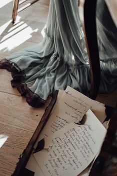 Aged suitcase with heap of letters with burned edges placed on wooden floor near crop faceless female in ling vintage skirt