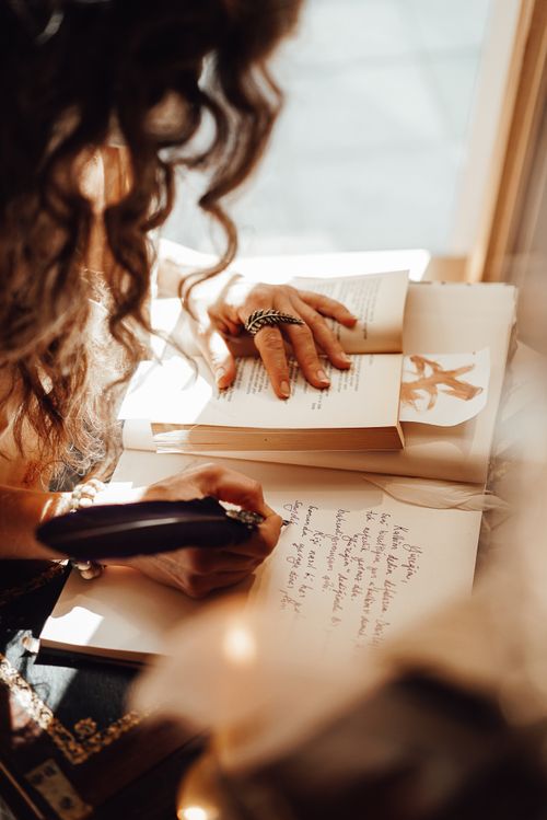 Free Crop unrecognizable female with curly hair taking notes with ink while sitting at vintage writing cabinet in retro style store with writing supplies Stock Photo