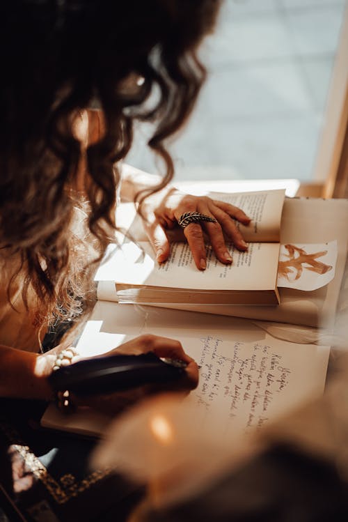 Free Crop anonymous female with dark hair sitting near window at retro writing cabinet while taking notes with feather in vintage store Stock Photo
