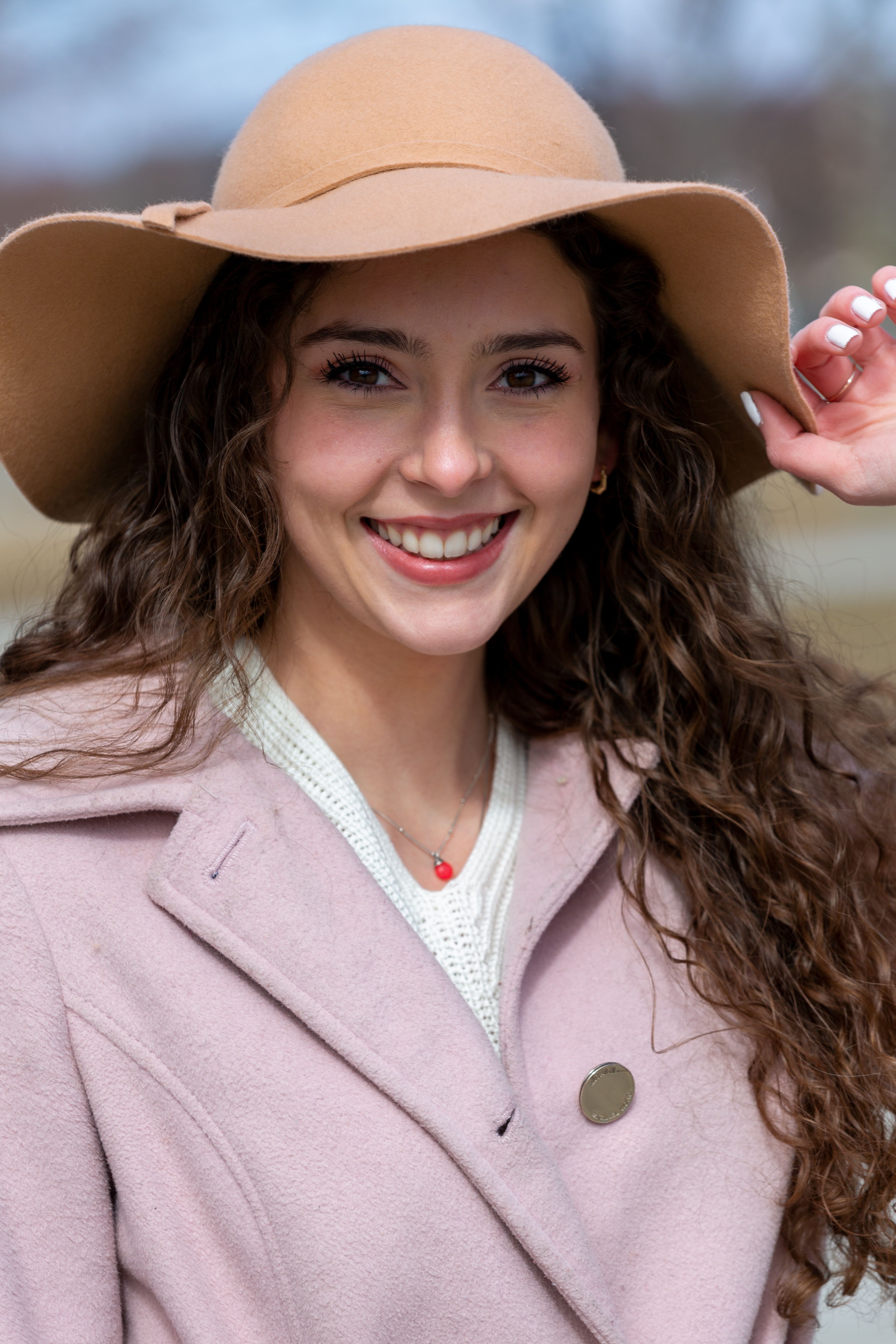 Beautiful woman smiling outdoors in a fashionable brown hat and pink coat.
