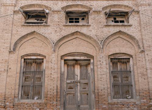 Free An old brick facade featuring arched windows and door with weathered textures. Stock Photo