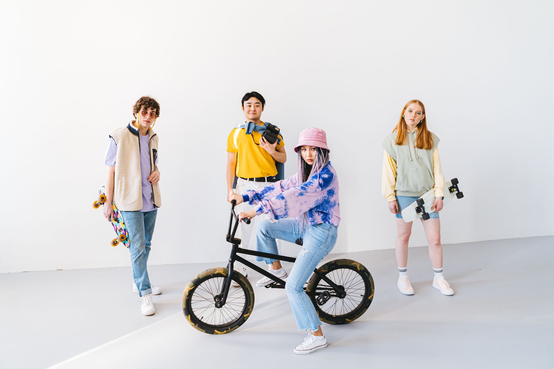 Dynamic group of teenagers in casual wear posing with BMX bike and skateboards indoors.