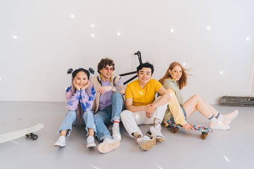 Free Group of diverse young friends sitting on the ground with skateboards indoors, smiling and relaxed. Stock Photo